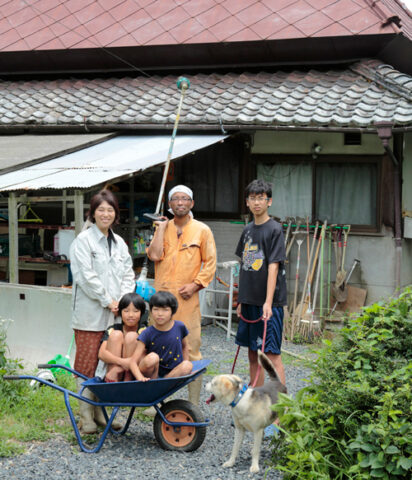 刈り払い機を担ぐ筆者と家族。7年前、当時小学生だった子どもたちの教育にもきっといいはずと移住を決意した