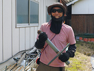 手に持っているのが自作のパイプ打ち込み器。直管パイプの上に被せて、ガンガン落とすとパイプが地面に刺さる。使い過ぎて鉄のキャップ（矢印）に穴があいてしまった